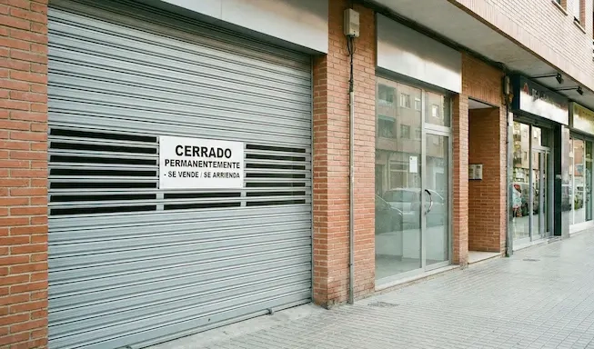 Fachada de un local comercial con reja abajo y aviso de cerrado, simbolizando el cierre de negocios